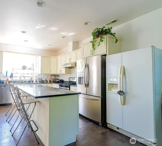 24003 21st Ave S, Des Moines, WA 98198 - kitchen featuring appliances with stainless steel finishes, under cabinet range hood, dark wood-style floors, a kitchen island, and white cabinets