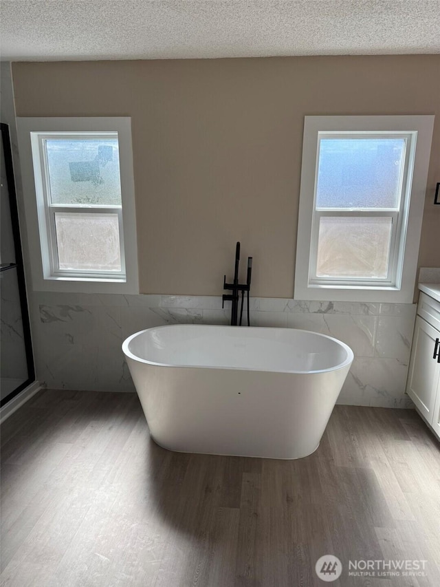 8102 195th St E Unit 95, Spanaway, WA 98387 - bathroom featuring tile walls, healthy amount of natural light, wood finished floors, vanity, and a freestanding tub