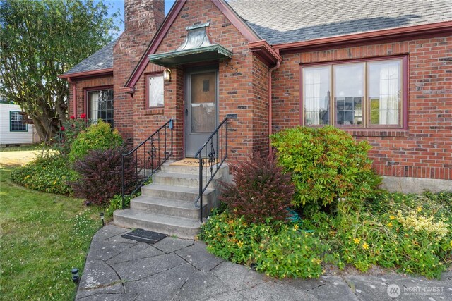 235 S 59th St, Tacoma, WA 98408 - view of exterior entry with a chimney, brick siding, and a shingled roof