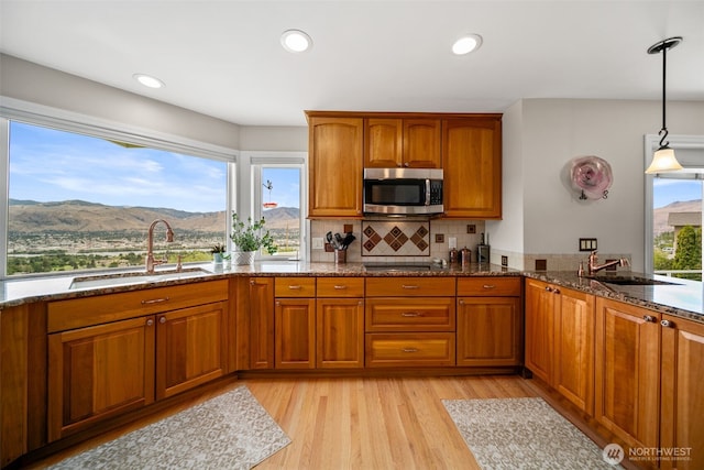 591 Daniels Dr NE, East Wenatchee, WA 98802 - kitchen featuring stainless steel microwave, brown cabinetry, dark stone counters, light wood-type flooring, and hanging light fixtures