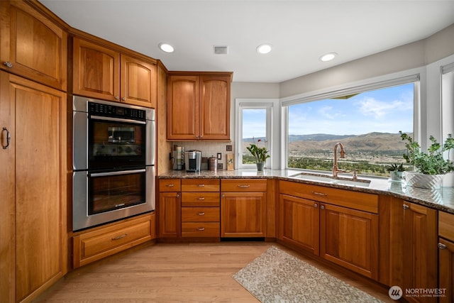 591 Daniels Dr NE, East Wenatchee, WA 98802 - kitchen featuring stainless steel double oven, dark stone countertops, brown cabinetry, a mountain view, and recessed lighting