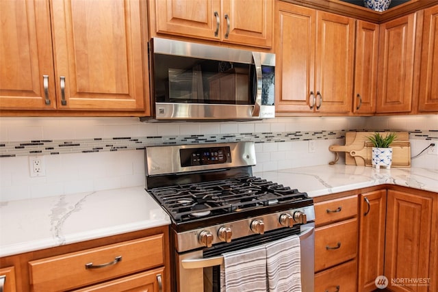120 Cascadia Loop, Sequim, WA 98382 - kitchen featuring stainless steel appliances, brown cabinets, tasteful backsplash, and light stone counters