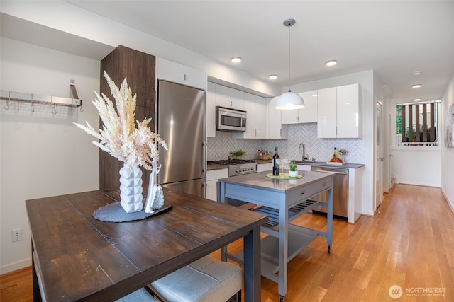 140 26th Ave E, Seattle, WA 98112 - kitchen featuring stainless steel appliances, white cabinets, backsplash, light wood finished floors, and pendant lighting