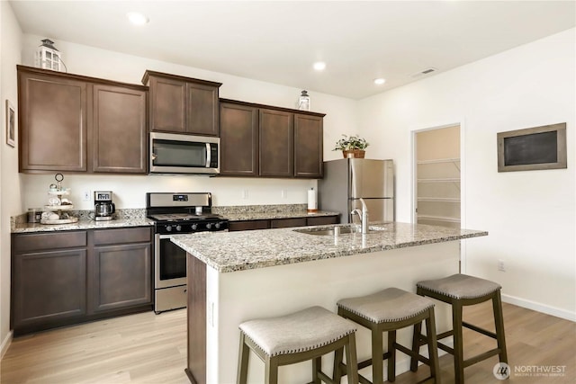 28515 76th Dr NW, Stanwood, WA 98292 - kitchen featuring appliances with stainless steel finishes, light wood-style flooring, a kitchen bar, a center island with sink, and dark brown cabinets