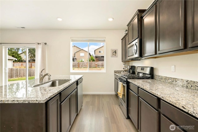 28515 76th Dr NW, Stanwood, WA 98292 - kitchen with stainless steel appliances, light wood-style floors, an island with sink, light stone counters, and dark brown cabinets