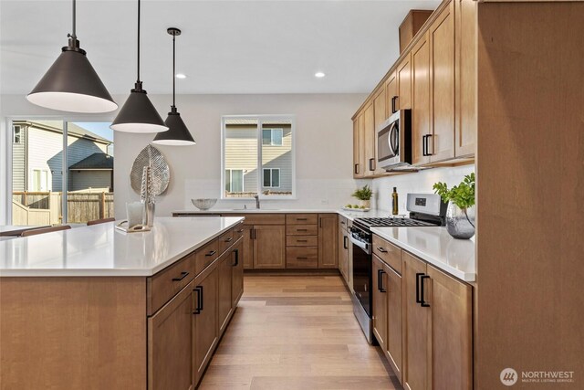 7164 91st St E, Puyallup, WA 98371 - kitchen with appliances with stainless steel finishes, light wood-style floors, light countertops, a center island, and hanging light fixtures