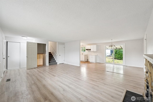 9442 S K St, Tacoma, WA 98444 - unfurnished living room featuring a textured ceiling, stairs, light wood-style floors, a stone fireplace, and a chandelier