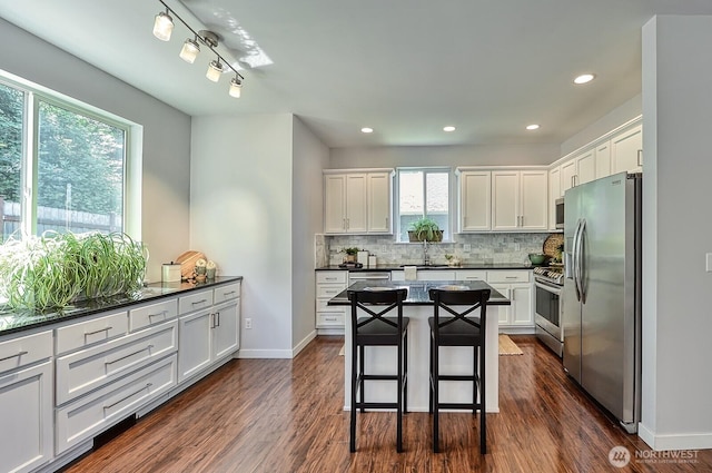 3606 Tree Farm Ct, Bellingham, WA 98226 - kitchen featuring appliances with stainless steel finishes, dark countertops, backsplash, white cabinetry, and a kitchen breakfast bar