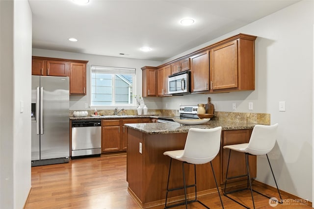 7436 S G St, Tacoma, WA 98408 - kitchen with appliances with stainless steel finishes, a peninsula, light wood finished floors, brown cabinetry, and recessed lighting