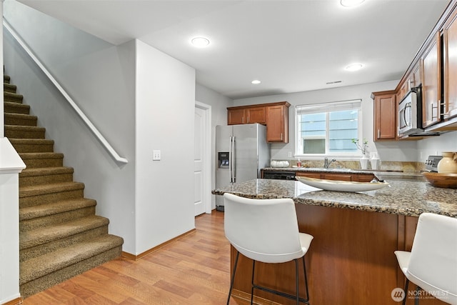 7436 S G St, Tacoma, WA 98408 - kitchen featuring stainless steel appliances, light wood-type flooring, a peninsula, dark stone counters, and brown cabinets