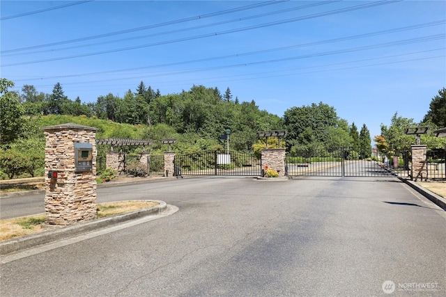 2711 SE 10th St Unit 1099, Renton, WA 98058 - view of asphalt road with a gate, a gated entry, curbs, and view of scattered trees