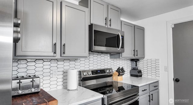 16228 Curry Ct SE, Yelm, WA 98597 - kitchen featuring stainless steel appliances, light stone countertops, backsplash, and gray cabinetry