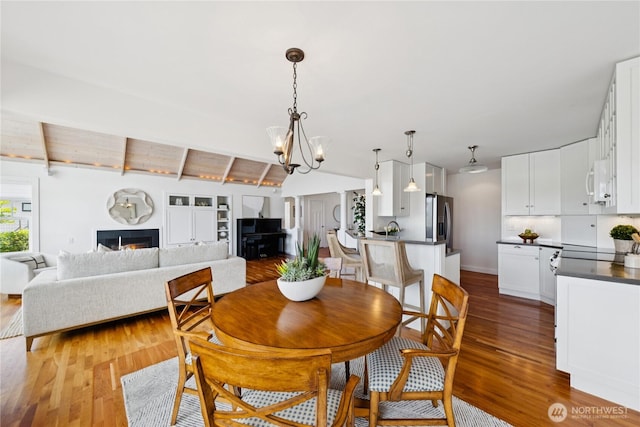 882 Shoshone Dr, La Conner, WA 98257 - dining space featuring wood finished floors, a chandelier, a lit fireplace, and beam ceiling