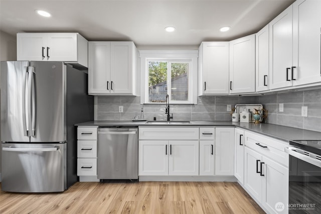 6416 S Huson St, Tacoma, WA 98409 - kitchen with appliances with stainless steel finishes, white cabinets, backsplash, light wood-style flooring, and dark countertops