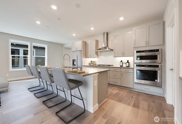 21725 SE 292 Nd Pl, Black Diamond, WA 98010 - kitchen with wall chimney exhaust hood, stainless steel appliances, light wood-style flooring, an island with sink, and a kitchen breakfast bar