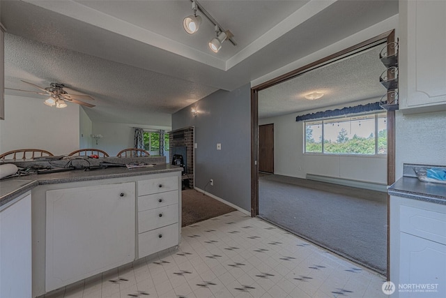 5735 NE 8th St, Renton, WA 98059 - kitchen featuring light colored carpet, white cabinets, a brick fireplace, a textured ceiling, and dark countertops