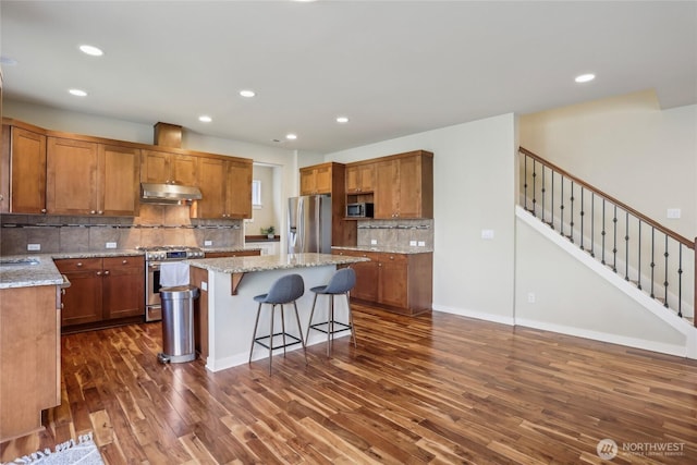 13218 106th Pl NE, Kirkland, WA 98034 - kitchen with stainless steel appliances, under cabinet range hood, dark wood-style floors, a center island, and brown cabinets