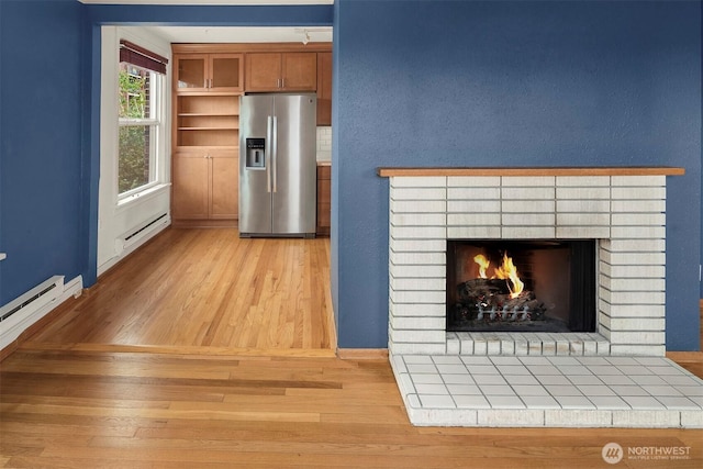 404 E Harrison St Unit 301, Seattle, WA 98102 - detailed view of stainless steel refrigerator with ice dispenser, wood finished floors, a brick fireplace, and baseboard heating