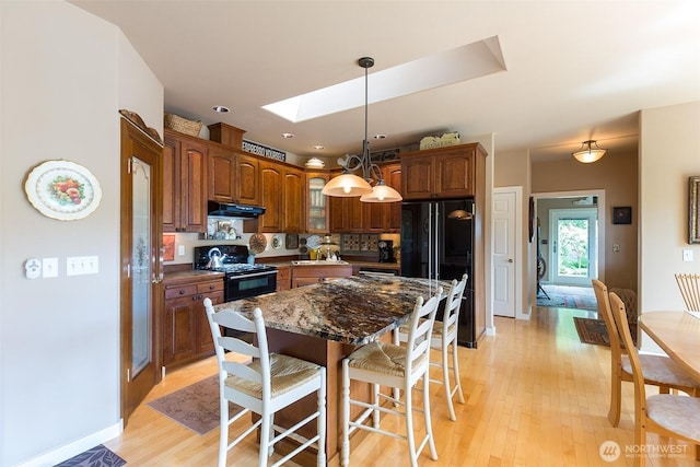 1901 W Hamilton Way, Port Angeles, WA 98363 - kitchen featuring black appliances, a skylight, a breakfast bar, under cabinet range hood, and light wood finished floors