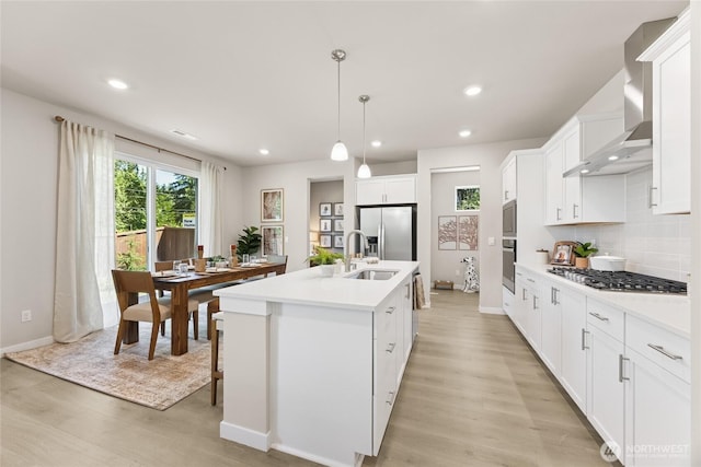 26808 NE 143rd Cir Unit 25, Duvall, WA 98019 - kitchen featuring appliances with stainless steel finishes, wall chimney range hood, light countertops, light wood-style flooring, and a center island with sink