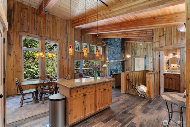 7189 Icicle Rd, Leavenworth, WA 98826 - kitchen with wood walls, dark wood-style floors, a wooden ceiling with exposed beams, a stone fireplace, and a kitchen island