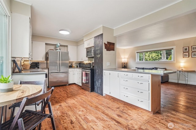1209 Yew St, Bellingham, WA 98229 - kitchen with appliances with stainless steel finishes, a peninsula, backsplash, light wood-style flooring, and white cabinets