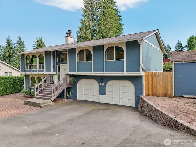 17837 Ashworth Ave N, Shoreline, WA 98133 - split foyer home featuring a garage, asphalt driveway, stucco siding, a chimney, and stairs