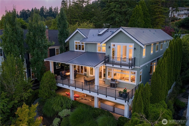 8066 Avalon Pl, Mercer Island, WA 98040 - back of house at dusk with a balcony, a standing seam roof, a metal roof, an attached garage, and a patio