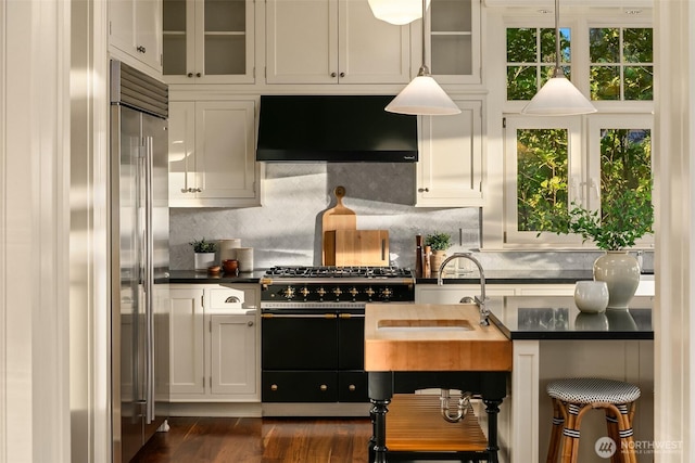 2665 Evergreen Point Rd NE, Medina, WA 98039 - kitchen with wall chimney exhaust hood, high quality appliances, dark countertops, glass insert cabinets, and white cabinetry