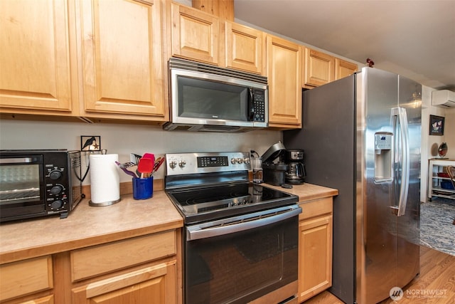 70 Onyx Ln, Sequim, WA 98382 - kitchen with appliances with stainless steel finishes, light brown cabinets, light countertops, a wall unit AC, and light wood-style floors