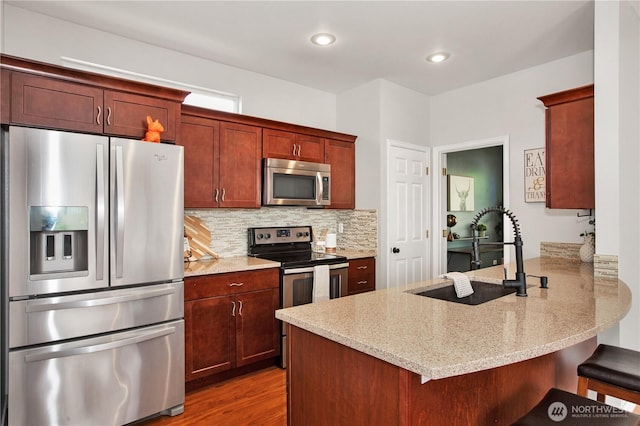 2025 Palisade Blvd, Dupont, WA 98327 - kitchen featuring appliances with stainless steel finishes, a peninsula, light stone counters, a breakfast bar area, and light wood finished floors