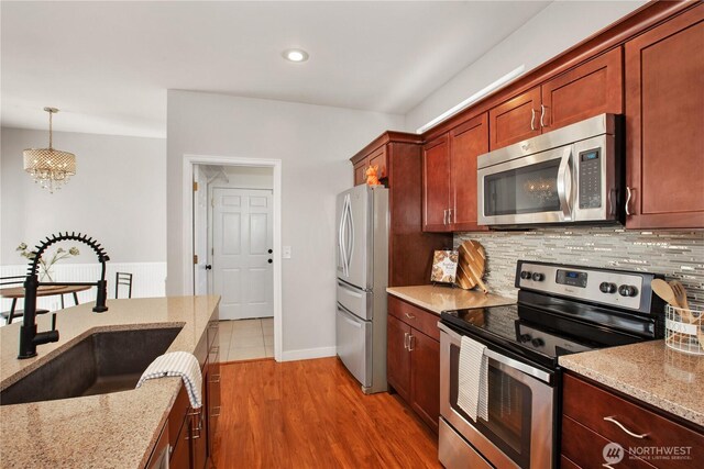 2025 Palisade Blvd, Dupont, WA 98327 - kitchen with appliances with stainless steel finishes, a chandelier, decorative backsplash, light stone counters, and decorative light fixtures