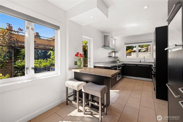 4315 52nd Ave NE, Seattle, WA 98105 - kitchen featuring wall chimney range hood, a peninsula, a breakfast bar area, dark cabinetry, and light tile patterned flooring