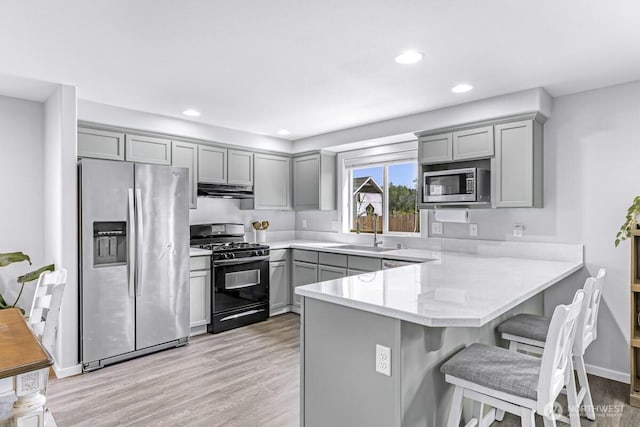 7308 Clamdigger Dr, Blaine, WA 98230 - kitchen featuring appliances with stainless steel finishes, gray cabinetry, under cabinet range hood, a peninsula, and recessed lighting