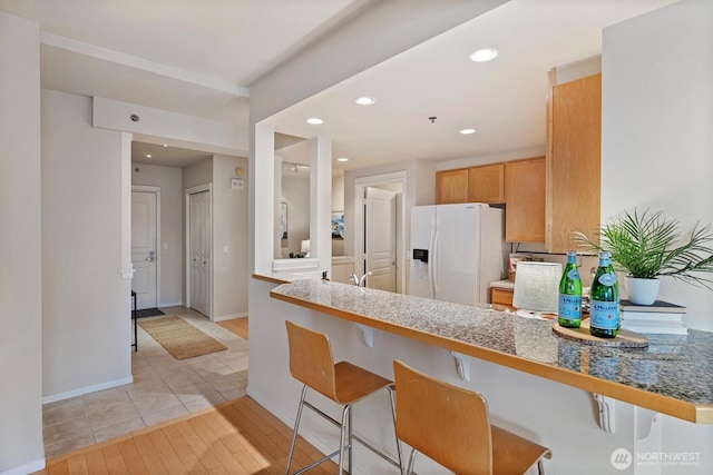 2801 1st Ave Unit 501, Seattle, WA 98121 - kitchen featuring white refrigerator with ice dispenser, a kitchen breakfast bar, tile countertops, recessed lighting, and light wood-style floors