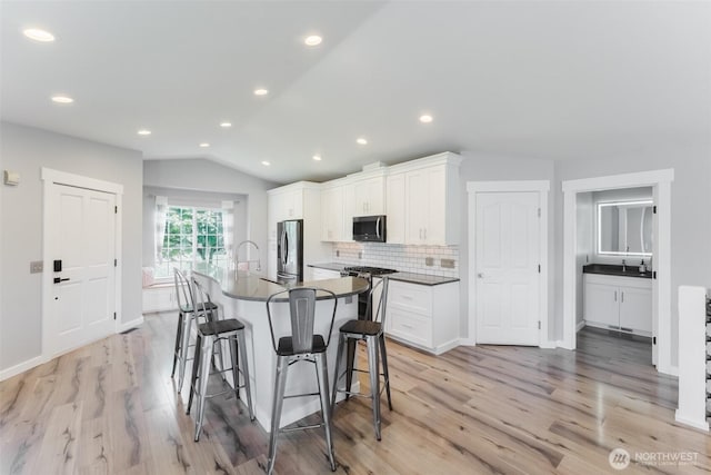 3761 Hannah Ct, Bellingham, WA 98226 - kitchen with appliances with stainless steel finishes, a kitchen bar, dark countertops, decorative backsplash, and light wood-type flooring