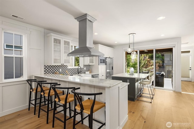 8841 Dibble Ave NW, Seattle, WA 98117 - kitchen with island range hood, a kitchen breakfast bar, tasteful backsplash, light wood-style flooring, and a peninsula