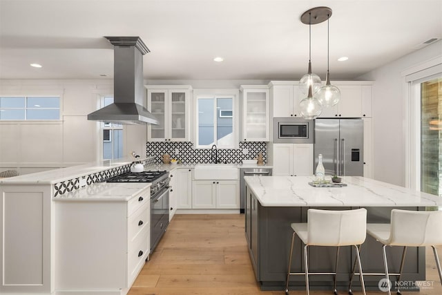 8841 Dibble Ave NW, Seattle, WA 98117 - kitchen featuring premium appliances, island exhaust hood, backsplash, light wood-style floors, and white cabinetry