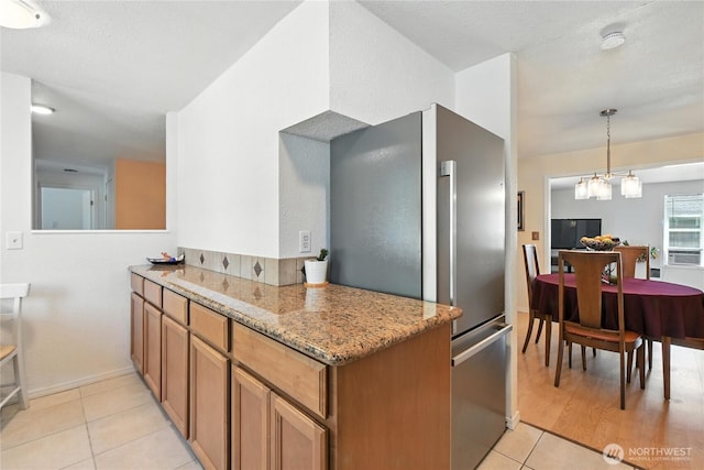 2102 35th Ave, Longview, WA 98632 - kitchen with freestanding refrigerator, light tile patterned floors, light stone counters, brown cabinets, and pendant lighting