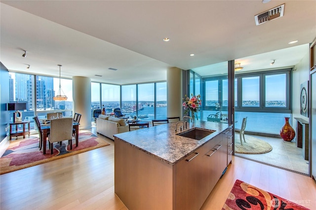 1521 2nd Ave Unit 2303, Seattle, WA 98101 - kitchen featuring light wood-style flooring, light stone countertops, an island with sink, open floor plan, and pendant lighting