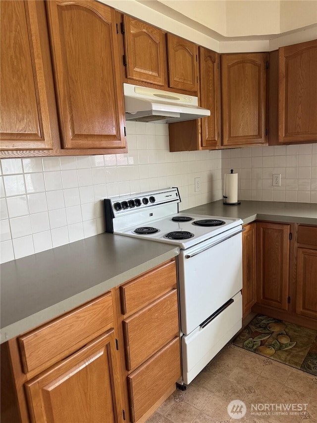 1019 Duryea St, Raymond, WA 98577 - kitchen featuring white electric stove, under cabinet range hood, backsplash, and brown cabinetry