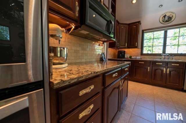 kitchen featuring light tile floors, tasteful backsplash, dark brown cabinetry, light stone counters, and sink