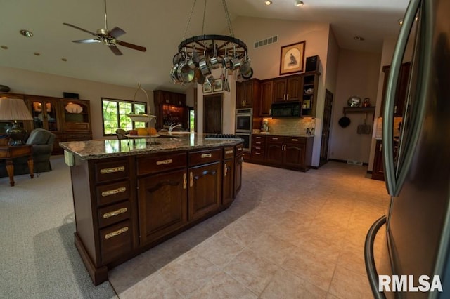 kitchen with an island with sink, dark stone counters, backsplash, black appliances, and ceiling fan with notable chandelier