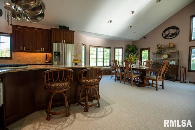 kitchen with stone counters, backsplash, a wealth of natural light, stainless steel refrigerator with ice dispenser, and light colored carpet