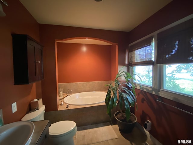 bathroom featuring tiled bath, sink, and toilet