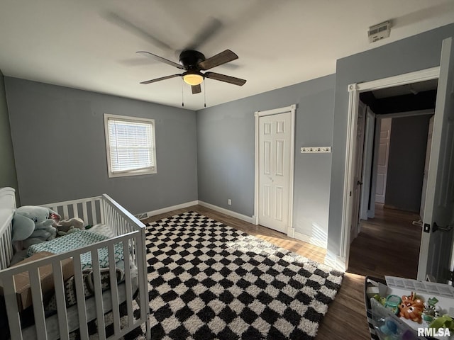 bedroom with ceiling fan, dark hardwood / wood-style flooring, and a nursery area