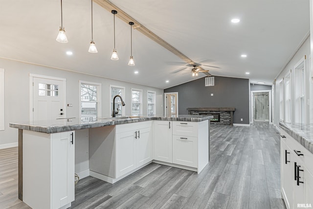 kitchen featuring vaulted ceiling, decorative light fixtures, white cabinetry, sink, and a kitchen island with sink