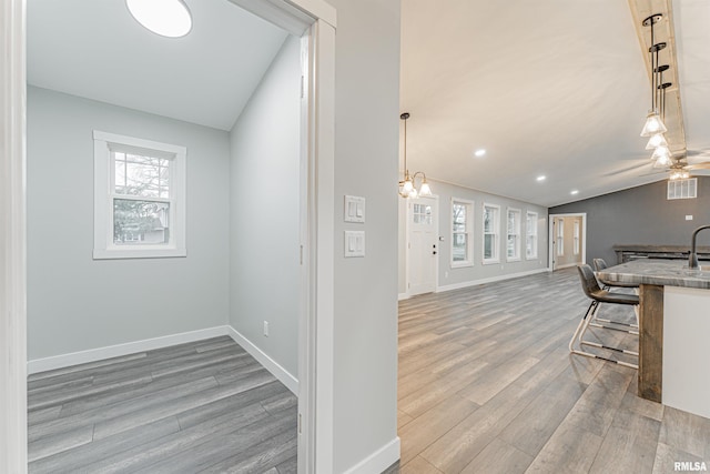 interior space featuring a breakfast bar, lofted ceiling, a chandelier, hanging light fixtures, and light hardwood / wood-style flooring