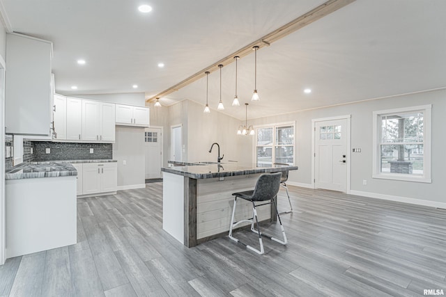 kitchen with decorative light fixtures, lofted ceiling with beams, tasteful backsplash, white cabinets, and a kitchen island with sink