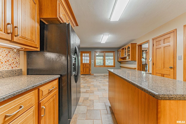 kitchen featuring black fridge, decorative backsplash, a center island, and stone counters